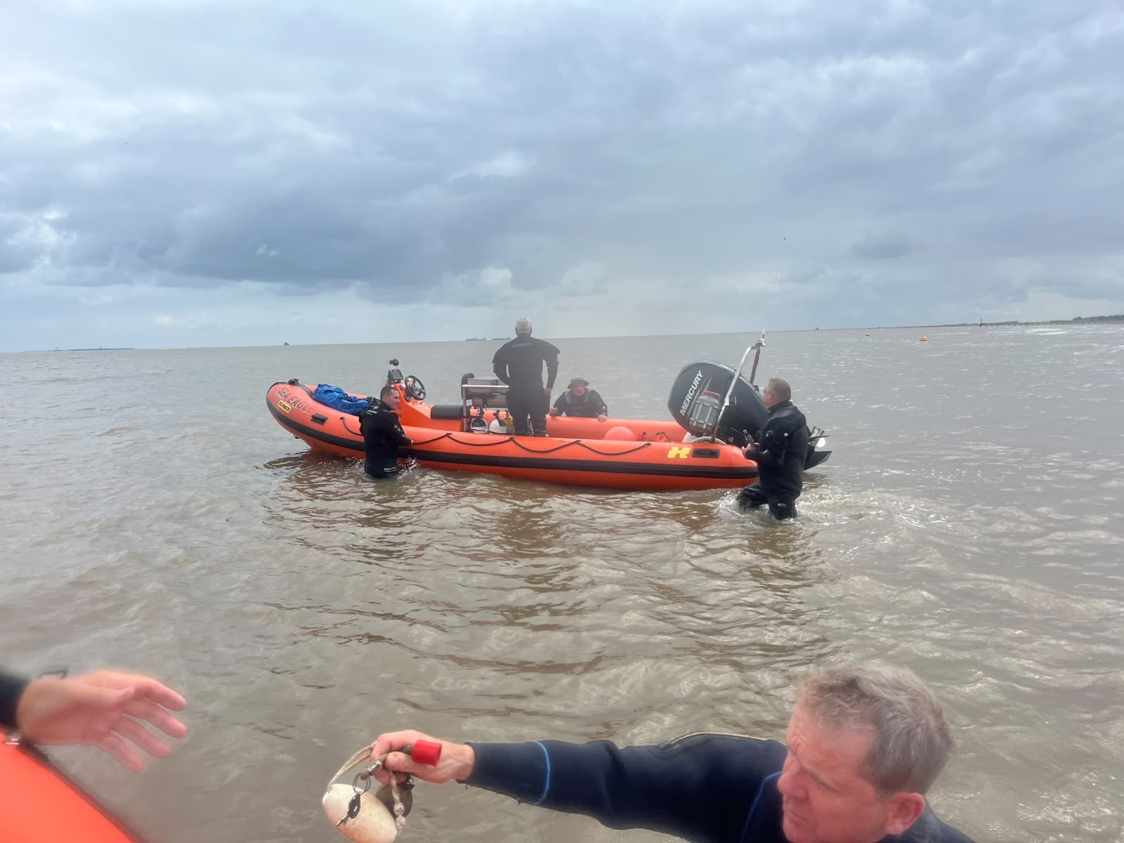 Divers standing beside an orange rigid inflatable boat in shallow water