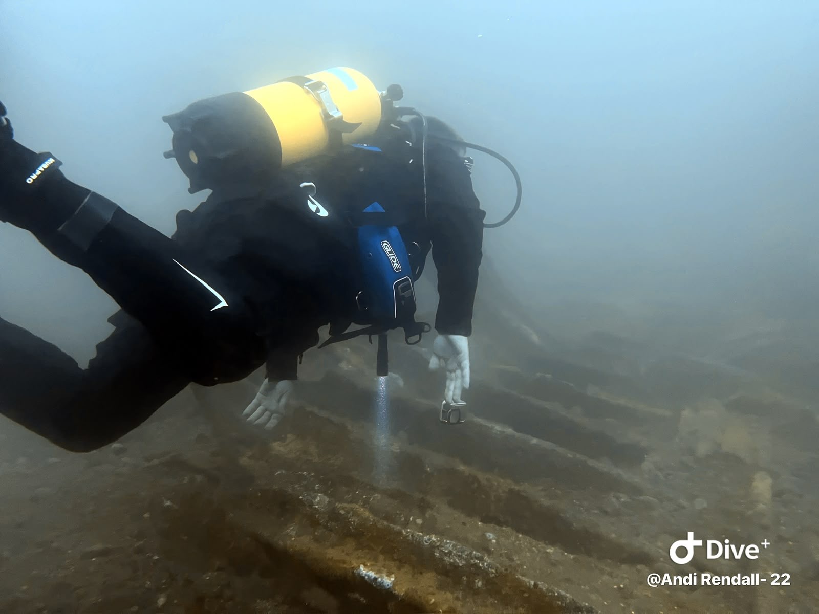 Diver with a yellow cylinder swimming above submerged wreckage